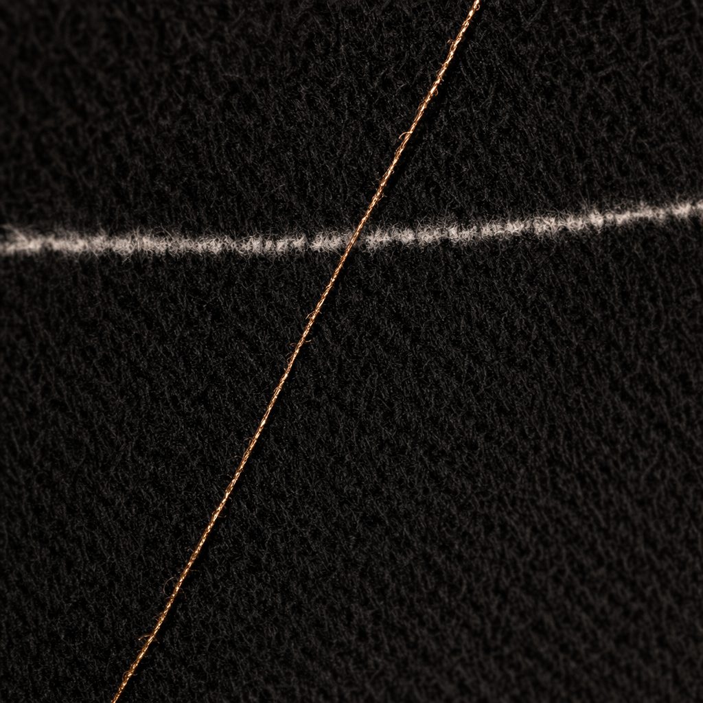 Macro detail of a chalk line across near-black wool cloth, marked with a single bronze thread